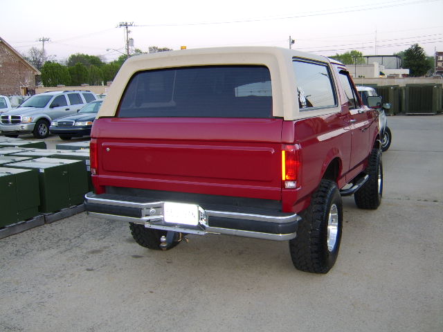 Red 1989 Ford Bronco rear view with tan top and aftermarket wheels