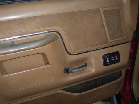 1989 Ford Bronco - Close-up of a vehicle's interior door panel, showing the armrest, door handle, and speaker grille.
