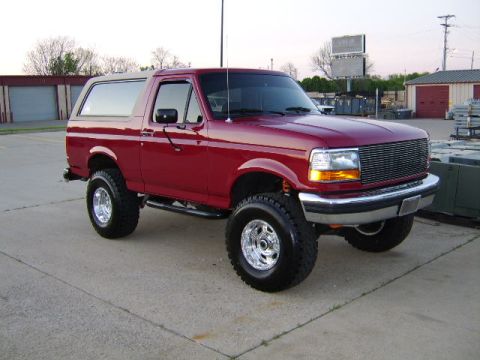 1989 Ford Bronco - This red 1992 Ford Bronco SUV is shown from a three-quarter front angle, a custom grille and lifted suspension.