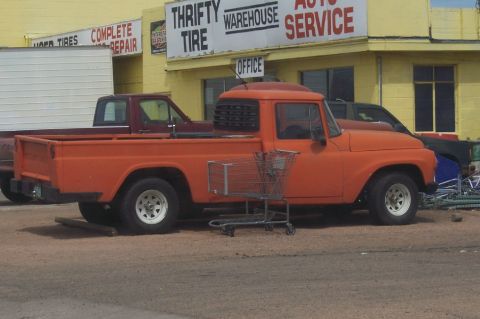 1972 Ford Ranchero - An orange pickup truck is parked in front of a yellow building with "Thrifty Tire" signage.