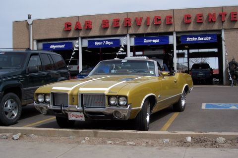 1972 Ford Ranchero - Gold convertible parked at a car service center, with an SUV to its left.