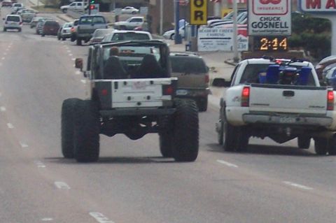 1972 Ford Ranchero - A lifted Jeep Wrangler with massive tires drives down the road, followed by a white pickup truck.