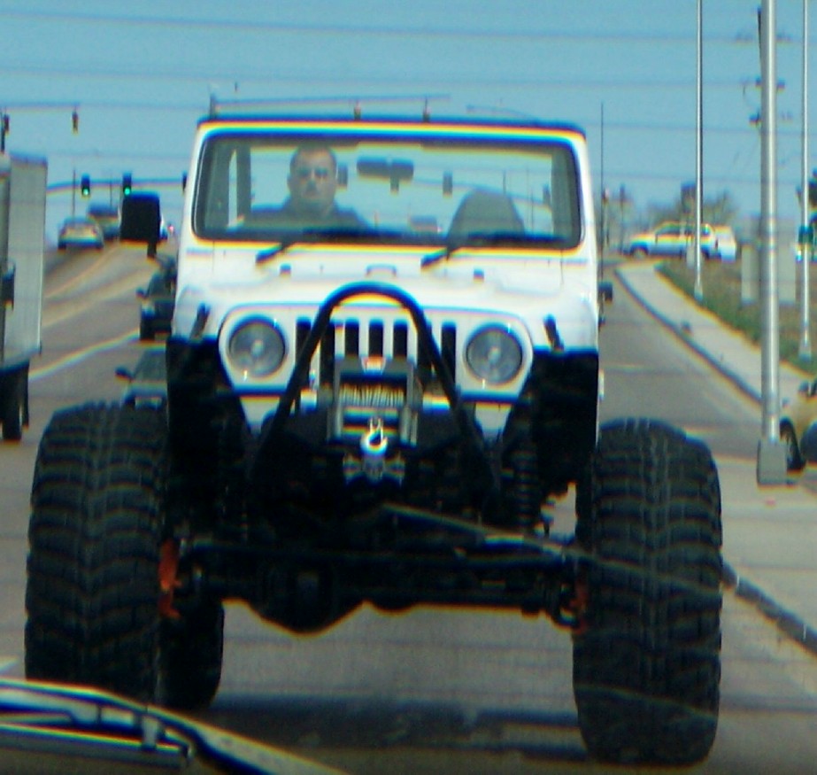 White Jeep Wrangler with huge tires and a winch on the front bumper driving on a road