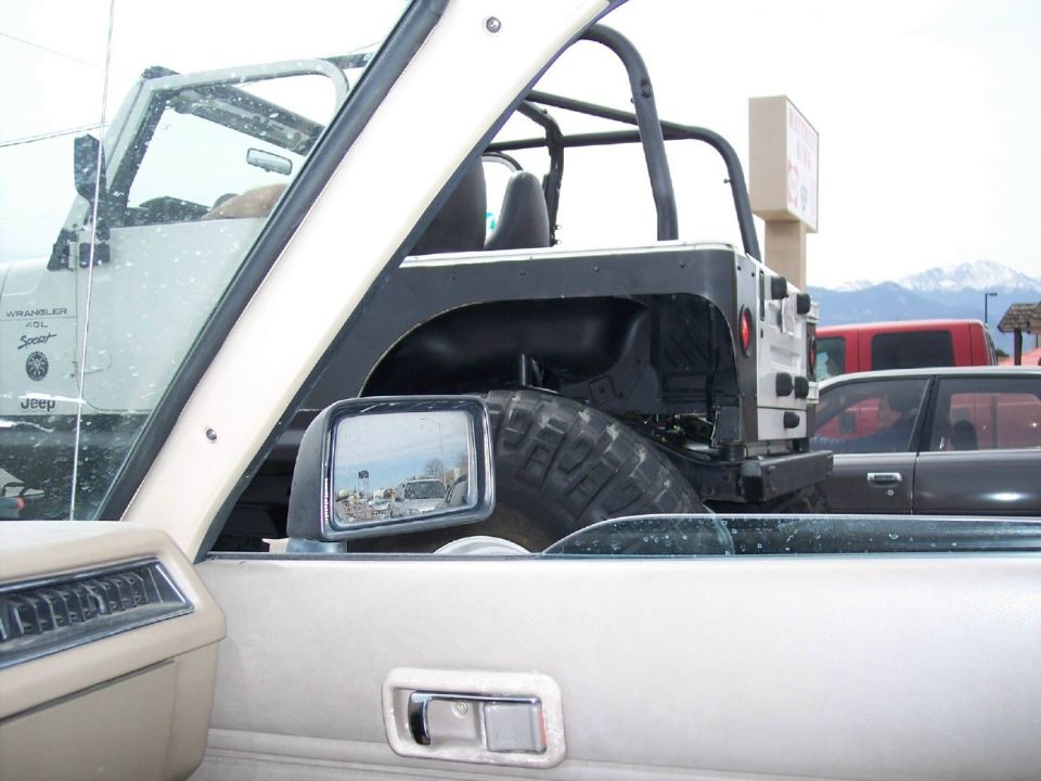 Jeep Wrangler interior with side mirror reflecting cars and a white Jeep Wrangler outside