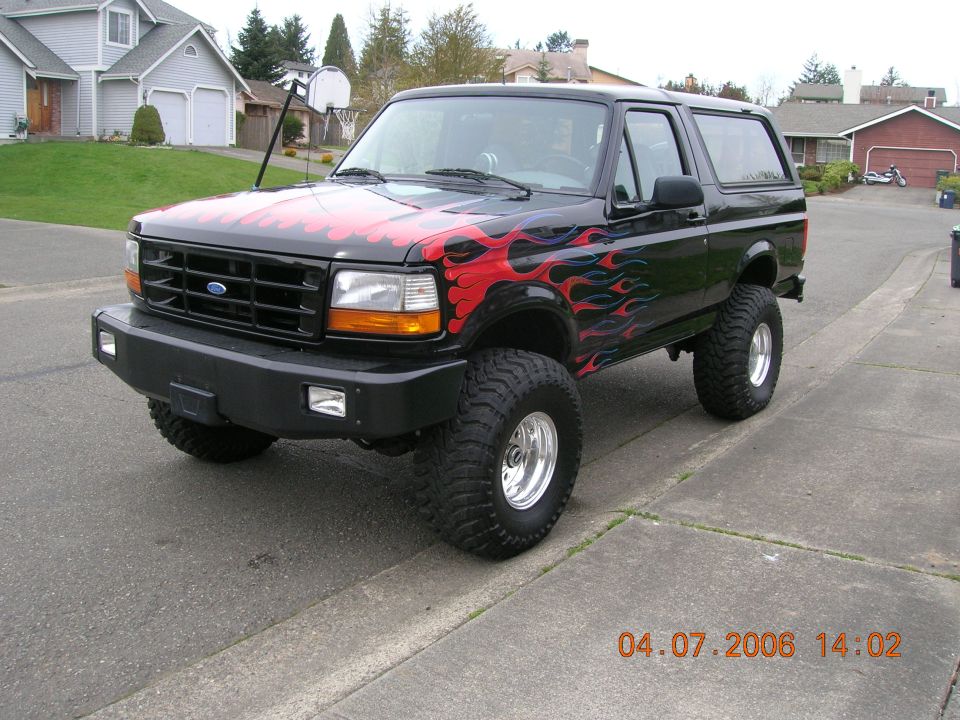 Black lifted Ford Bronco with red and blue flame graphics on a driveway, front three-quarter view