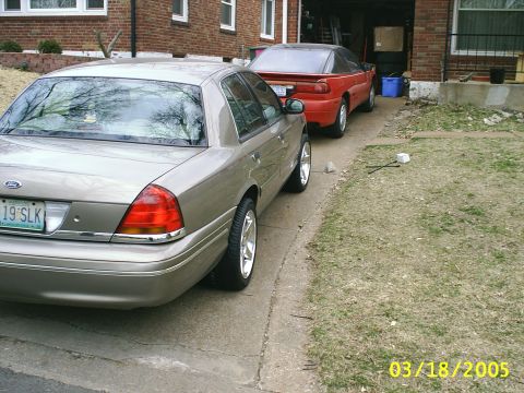 2000 Ford Crown Victoria - A tan Ford Crown Victoria is parked in a driveway next to a red coupe.