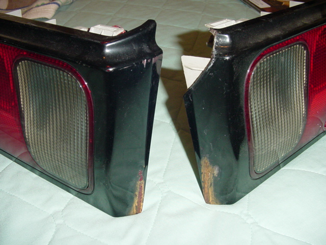 Two removed taillight assemblies with red and smoked lenses on a quilted blanket, showing paint wear