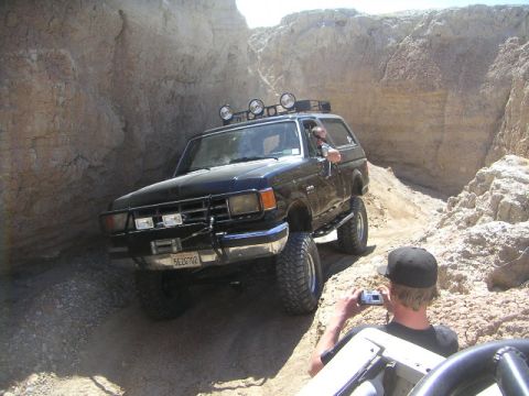 1988 Ford Bronco - A black Ford Bronco navigates a narrow, rocky off-road trail with a person filming from another vehicle.