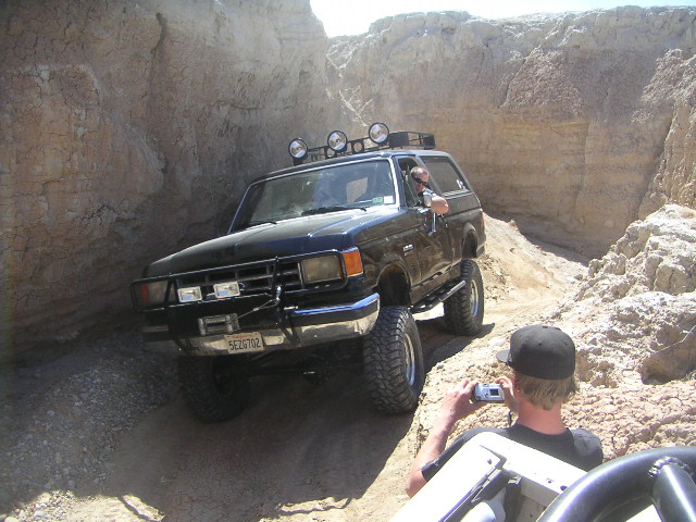 Black Ford Bronco with off-road tires and light bar driving through a rocky canyon