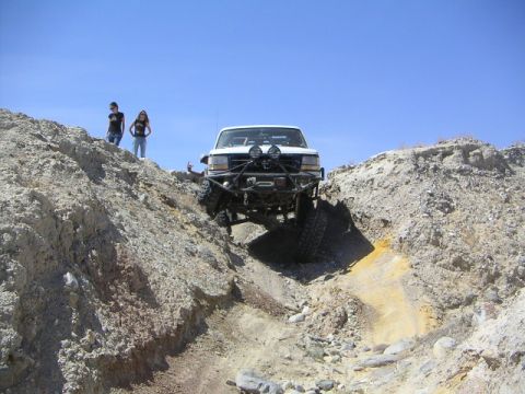 1988 Ford Bronco - This modified truck navigates a challenging off-road trail under a clear blue sky.