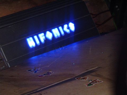 1994 Ford Thunderbird - A car amplifier with a glowing blue logo sits on a wooden surface adorned with stickers.