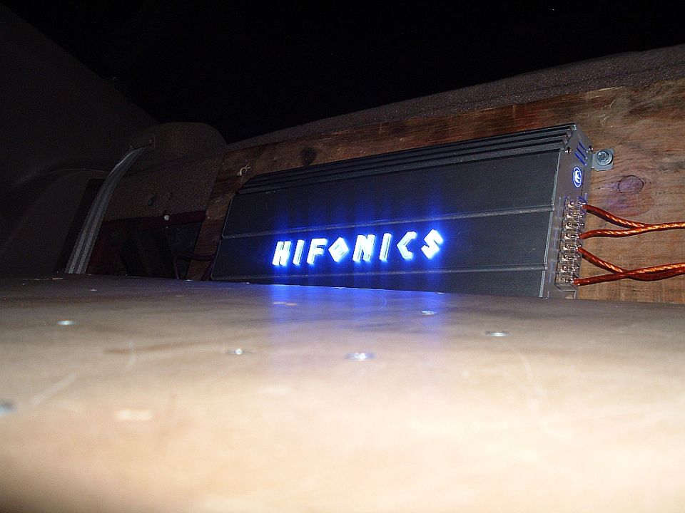 HIFONICS car amplifier with blue illuminated logo, mounted on wood