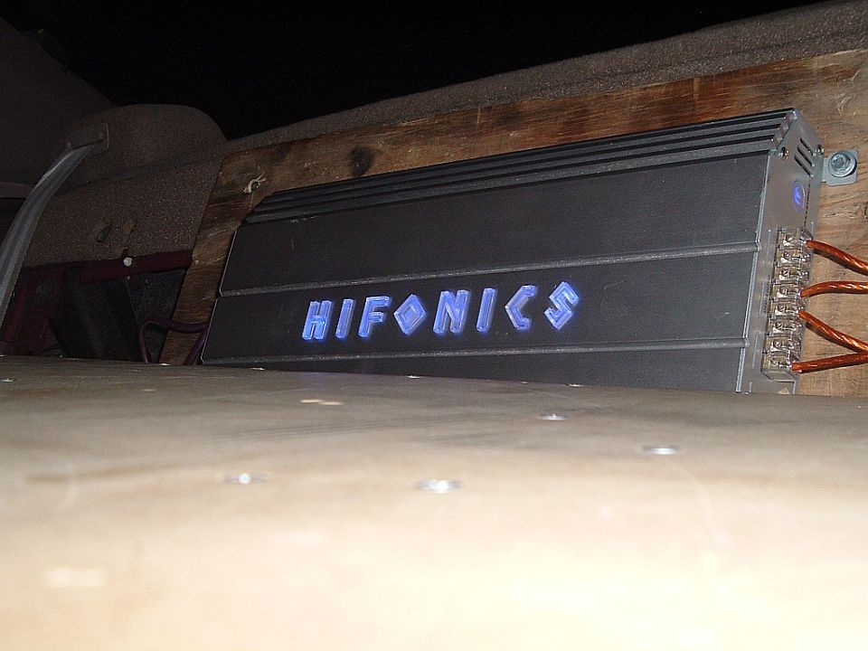Hifonics car audio amplifier with blue illuminated logo, mounted on wood paneling