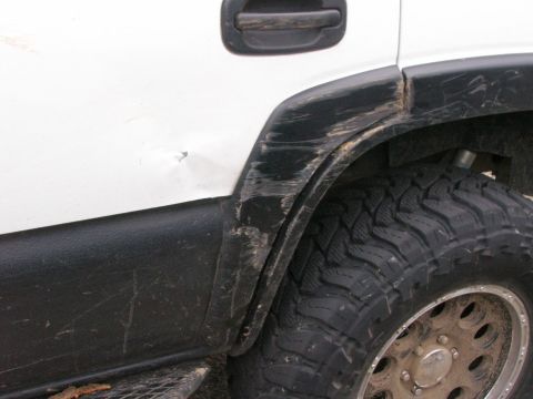 2002 GMC Yukon - Close-up of the rear side of a white 2002 GMC Yukon, showing wear and tear on the fender.