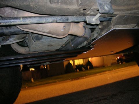 2002 GMC Yukon - Vehicle underbody showing exhaust system and skid plate. A distant SUV is visible.