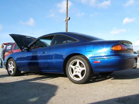 1996 Ford Probe - A blue coupe is parked with its hood open, seen from the rear 3/4 angle. Another vehicle is partially visible in the background.