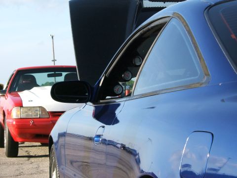 1996 Ford Probe - Two cars are parked side-by-side with their hoods open, showing gauges inside the blue car.