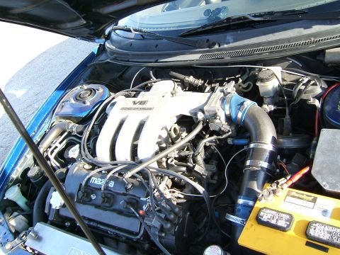 1996 Ford Probe - The engine bay of a blue car shows a V6 engine with "Mazda" branding and a "SUPERMOTORS" watermark.