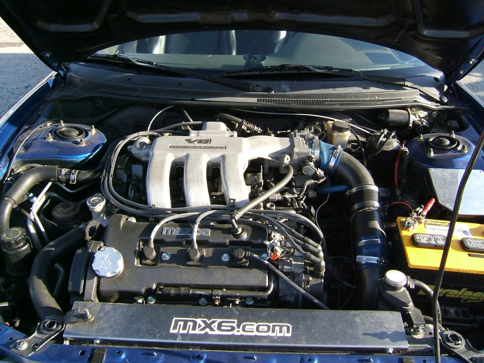 Mazda MX-6 engine bay with V6 intake manifold and "mx6.com" sticker on radiator cover