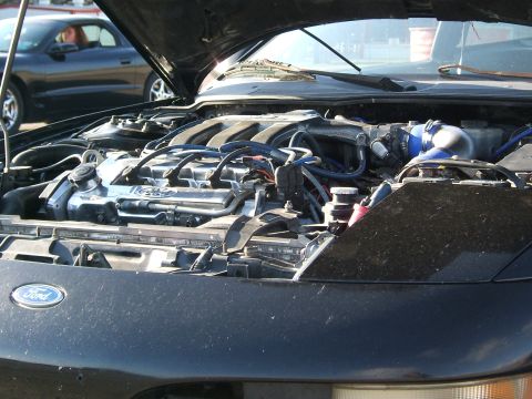 1996 Ford Probe - The engine bay of a black car is shown, with a Ford logo on the front. Another vehicle is visible in the background.