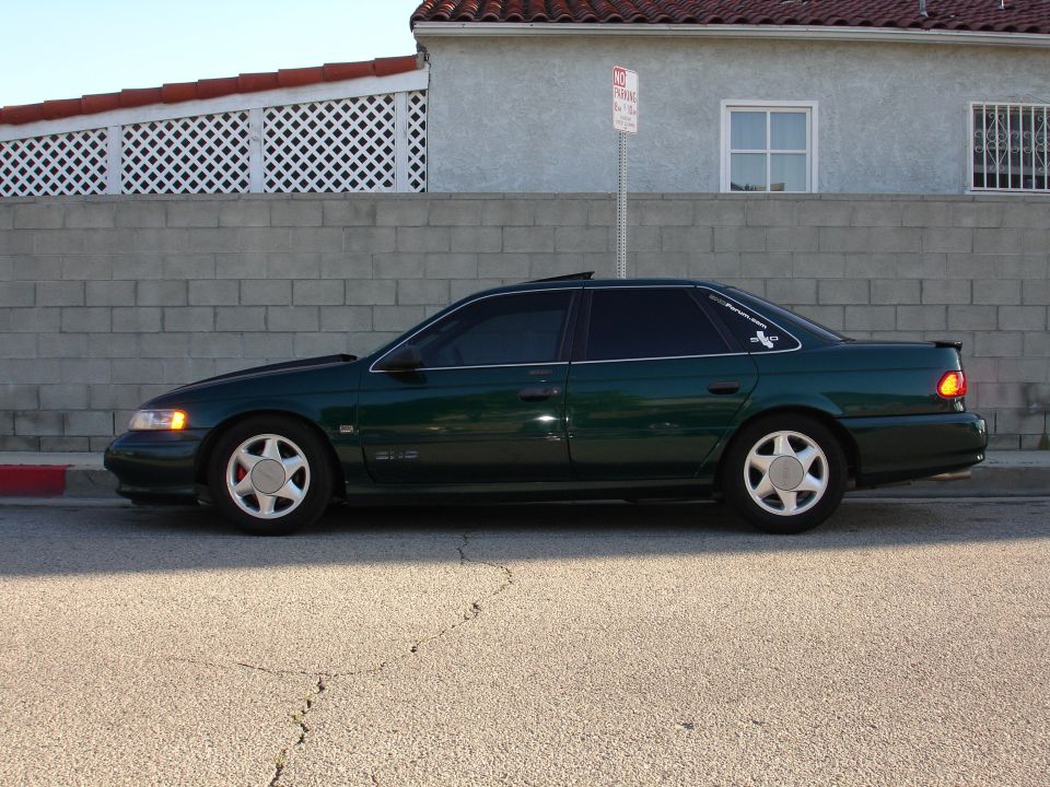 1993 Ford Taurus sedan, side view, dark green paint, tinted windows, parked on asphalt