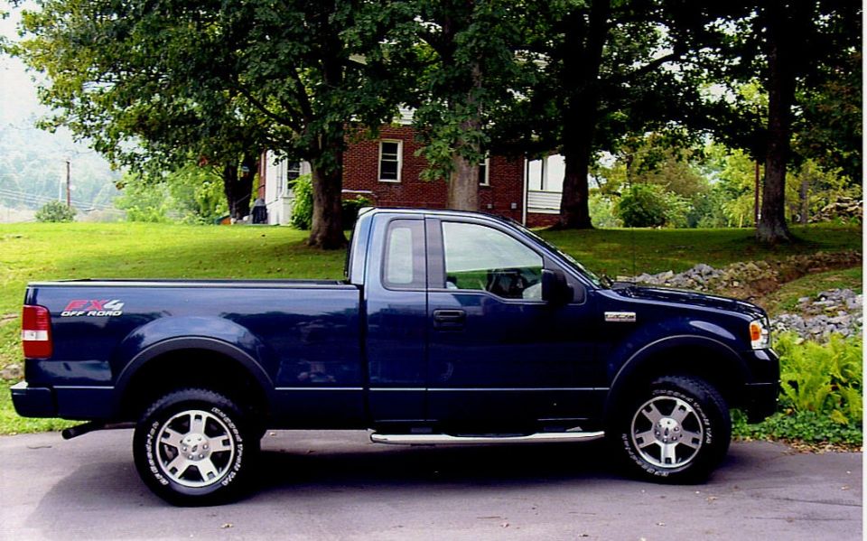 Dark blue 2004 Ford F-150 FX4 pickup truck, side view, parked on asphalt with trees and a house in the background