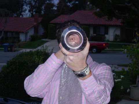 1998 Ford Crown Victoria - A person holds a large chrome exhaust tip up to their face, looking through it.