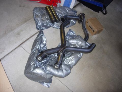 1998 Ford Crown Victoria - Unwrapped exhaust system components are laid out on a garage floor next to a cardboard box.
