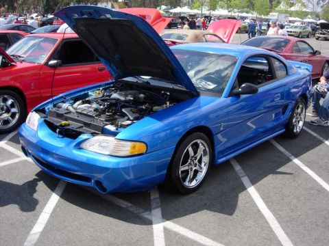 1998 Ford Crown Victoria - A blue coupe with its hood open, revealing the engine, parked at an outdoor event.