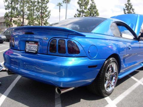 1998 Ford Crown Victoria - Rear view of a blue Ford Mustang, showing custom taillights and a spoiler. Chrome wheels are visible.