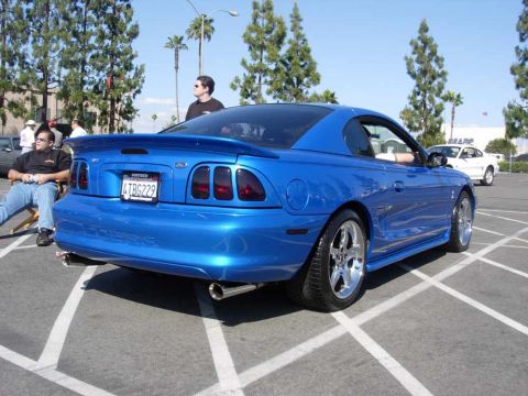 1998 Ford Crown Victoria - A blue 1998 Ford Mustang Cobra is parked in a lot, with another white car visible in the background.