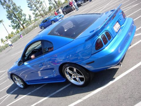 1998 Ford Crown Victoria - A blue coupe with a spoiler and custom wheels is parked in a lot.