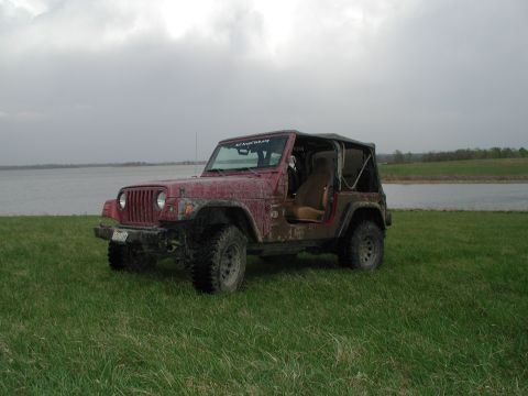 1998 Jeep TJ - This red Jeep Wrangler is parked on a grassy area next to a lake under a cloudy sky.