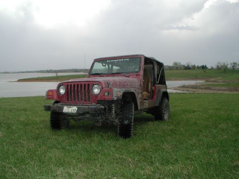 1998 Jeep TJ - This Jeep Wrangler is parked in a grassy field with a cloudy sky overhead and a body of water in the background.
