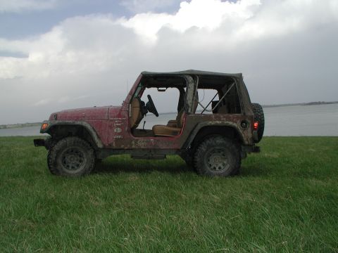 1998 Jeep TJ - A red Jeep Wrangler sits on a grassy field with a cloudy sky overhead and a body of water in the background.