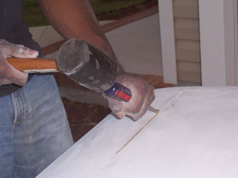 1978 Ford Bronco - A person is working on a fiberglass part with a chisel and mallet.