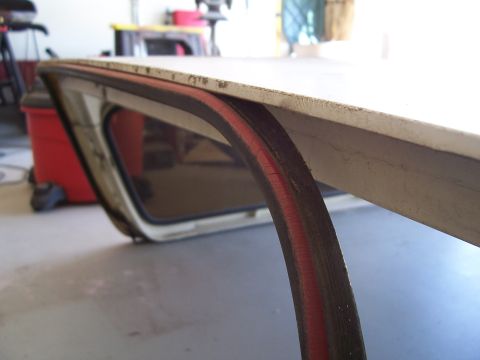 1978 Ford Bronco - Low-angle close-up along the front edge of a removed white fiberglass hardtop resting on a garage floor, showing the black rubber weatherst…