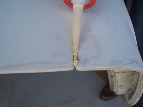 1978 Ford Bronco - A caulk gun applies sealant to a seam on a light-colored fiberglass panel.