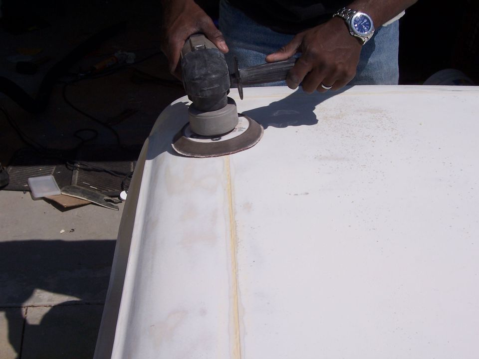Person sanding a white fiberglass part with a power sander