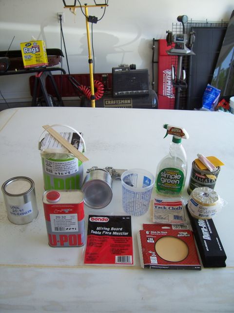 1978 Ford Bronco - Various automotive repair supplies are laid out on a white surface, including Bondo, tack cloth, and spray cleaner.