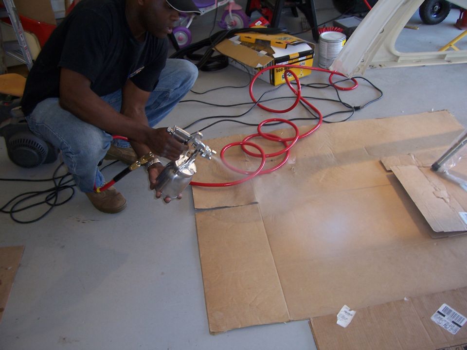 Man spray painting a part with a spray gun and red hose