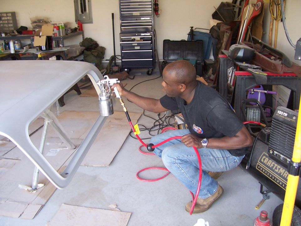 Man in jeans and t-shirt spray painting a car roof supported by sawhorses in a garage