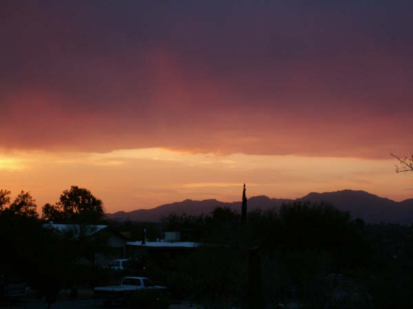 White pickup truck rear view, parked in silhouette against a sunset sky with mountains and houses