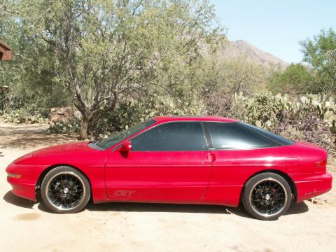 1995 Ford Probe - Side view of a red coupe with black rims and a GT badge, parked outdoors.