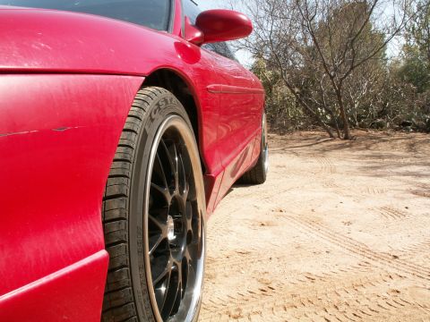 1995 Ford Probe - A red sports car is parked on a dirt road with dry brush and trees in the background.