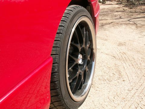 1995 Ford Probe - Side view of a red car's wheel and fender, showing aftermarket rims.