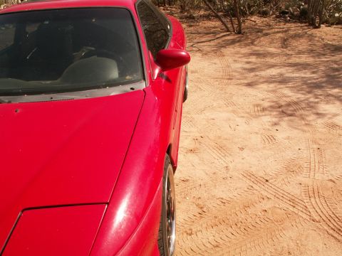 1995 Ford Probe - A red sports coupe is parked on a dirt surface with tire tracks visible in the background.