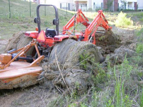 1995 Ford Bronco - An orange tractor is deeply stuck in mud, with its loader arm digging into the earth.