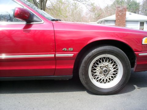 1995 Ford Crown Victoria - Close-up of a red sedan's front fender, showing the '4.6' engine badge and a wire-spoke wheel.