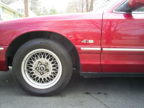 1995 Ford Crown Victoria - Close-up of a red car's fender, showing a 4.6 badge and a distinctive wire wheel.